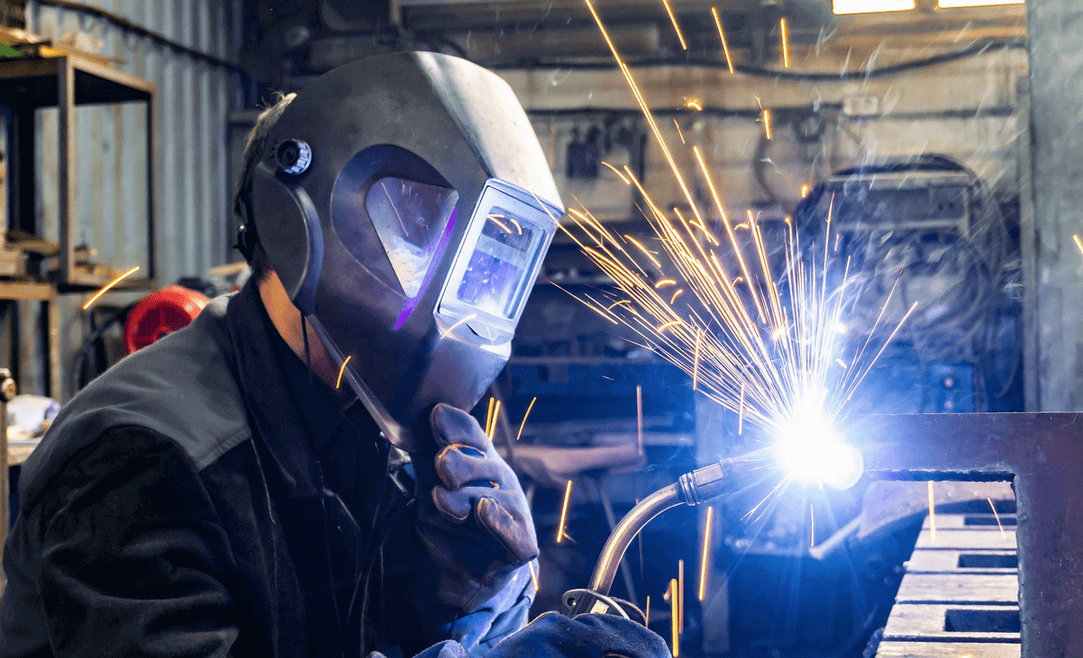 A man performing welding in a factory, demonstrating precision and safety while working with metal materials and tools.