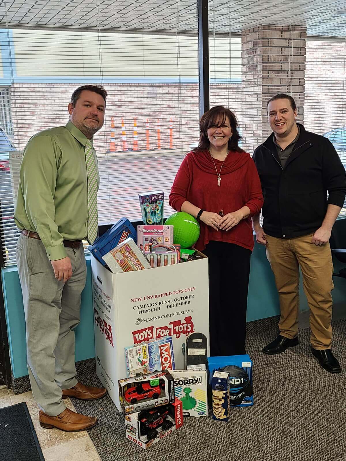 A large box of toys is surrounded by three people, highlighting their engagement with the colorful collection of toys.