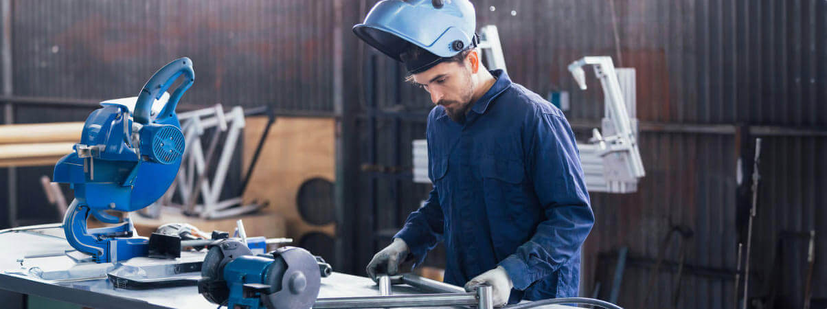 A man wearing a blue shirt and blue helmet is focused on his work at a table.